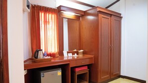 A compact hotel room with a wooden desk, a small refrigerator, a mirror, and a wardrobe.