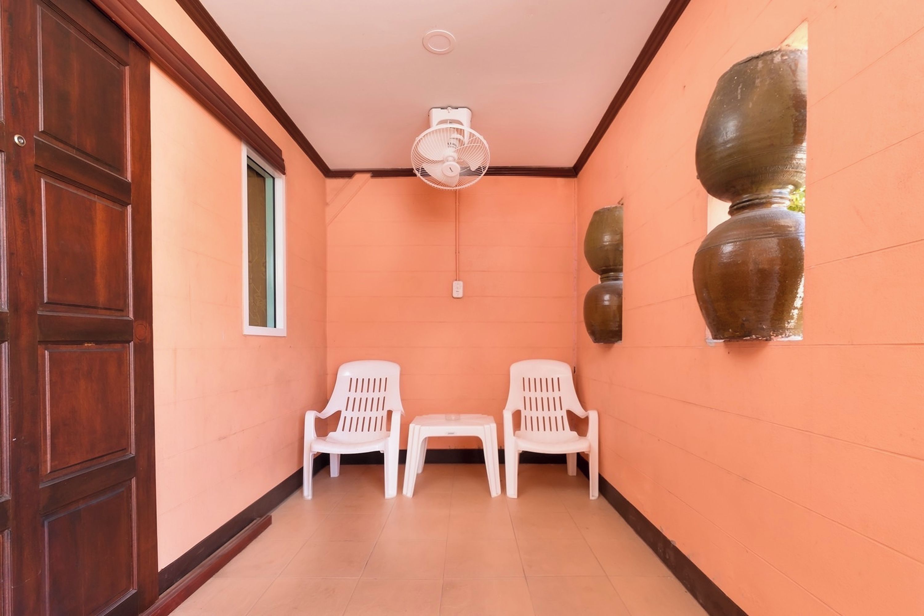 A hallway with two white plastic chairs, a ceiling fan, and a wall-mounted vase.