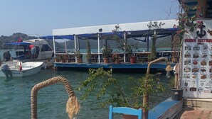 A wooden table with blue chairs at a waterfront restaurant with potted plants and a menu board. - Kekova Restaurant & Pansiyon (Demre)