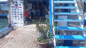 A nautical-themed restaurant with a blue and white color scheme, a signboard listing menu items, and a staircase leading to the upper deck. - Kekova Restaurant & Pansiyon (Demre)