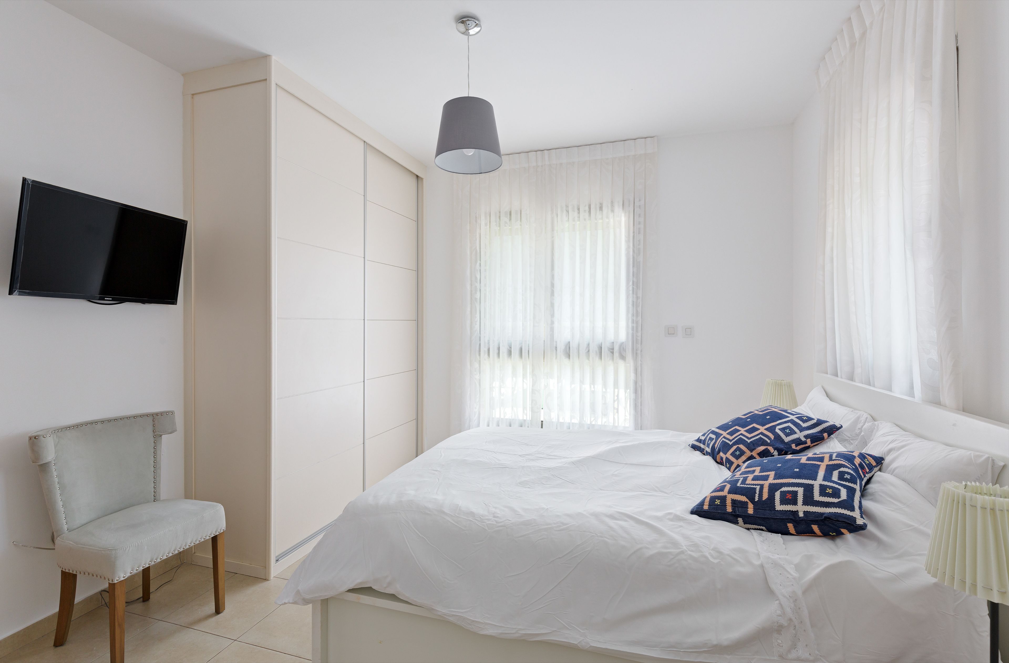 Una camera da letto con un letto, una sedia, una televisione e una finestra con tende.