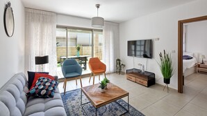 A modern living room with a sofa, armchairs, a coffee table, a TV, and a dining area with a table and chairs. - Laguna Water Front 1 (Herzliya)