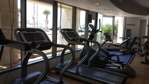 A gym with treadmills, exercise bikes, and a large window providing natural light. - Laguna Water Front 1 (Herzliya)