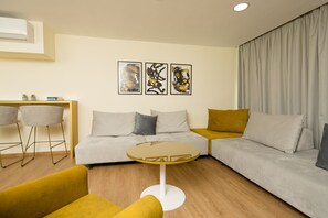 Una sala de estar moderna con un sofá, una mesa redonda de vidrio y dos sillones. Hay tres cuadros abstractos en la pared.