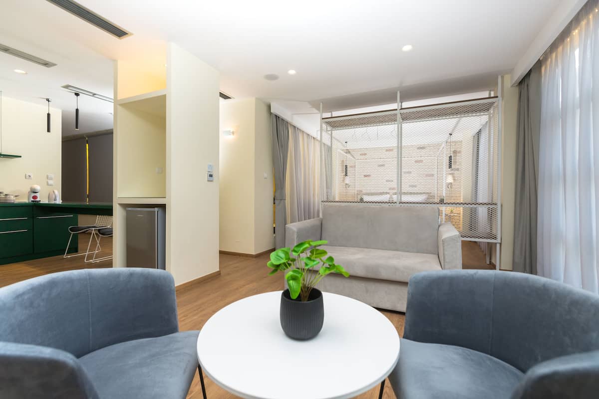 Uma sala de estar moderna com uma mesa redonda branca, duas poltronas cinzas, um sofá cinza, uma planta em vaso e uma grande janela com cortinas.