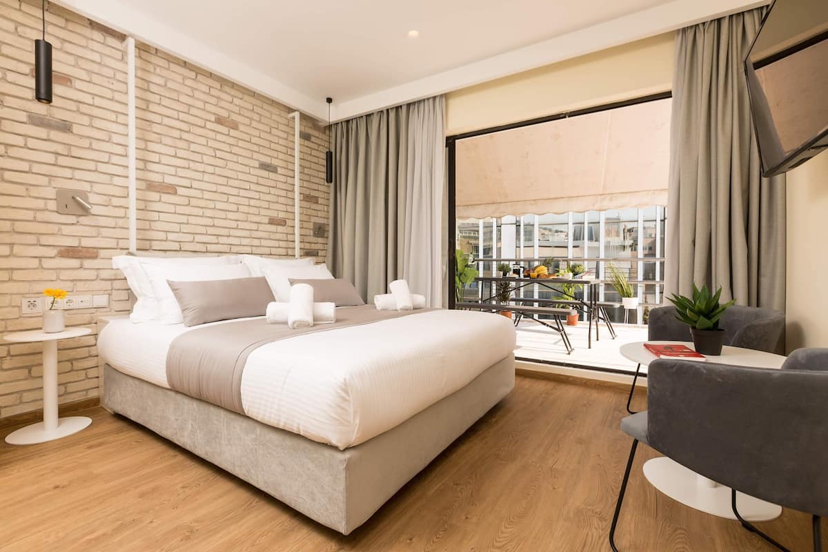 Quarto de hotel moderno com uma cama grande, uma mesa pequena, uma cadeira e varanda com vista.