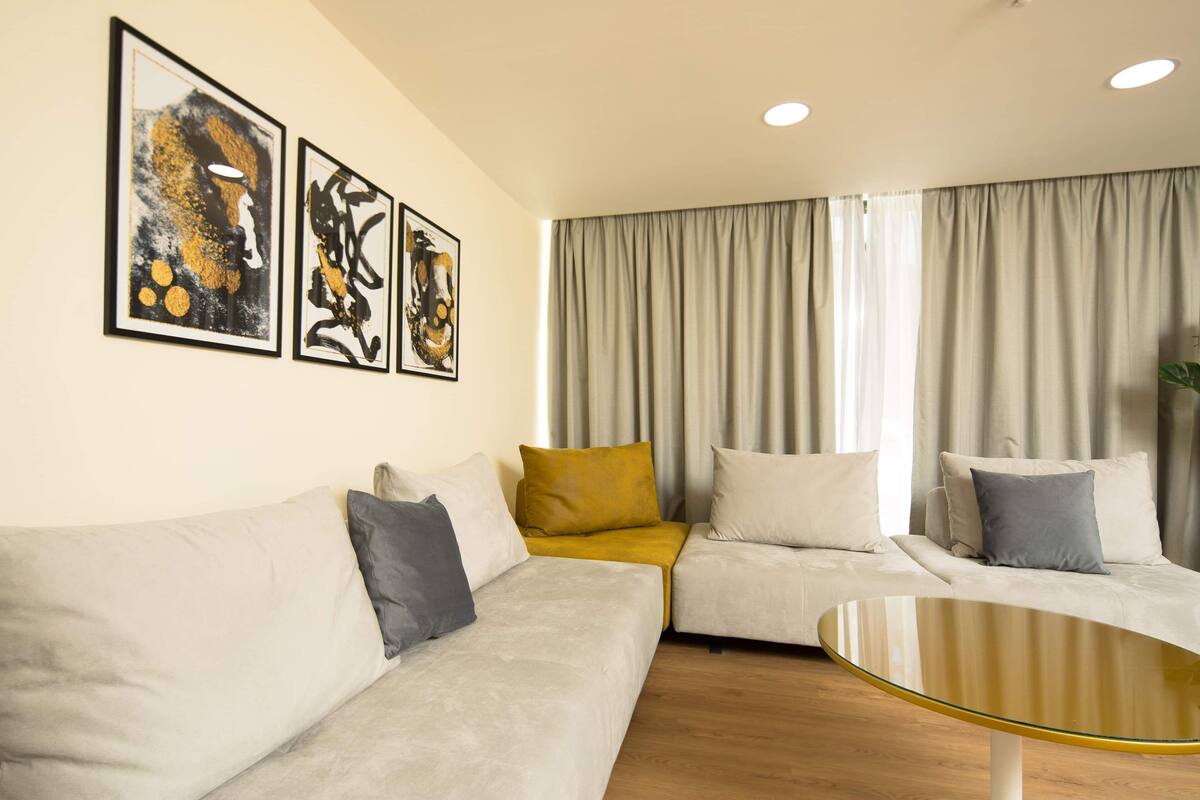 Uma sala de estar moderna com um sofá seccional, uma mesa de centro de vidro e arte abstrata na parede.