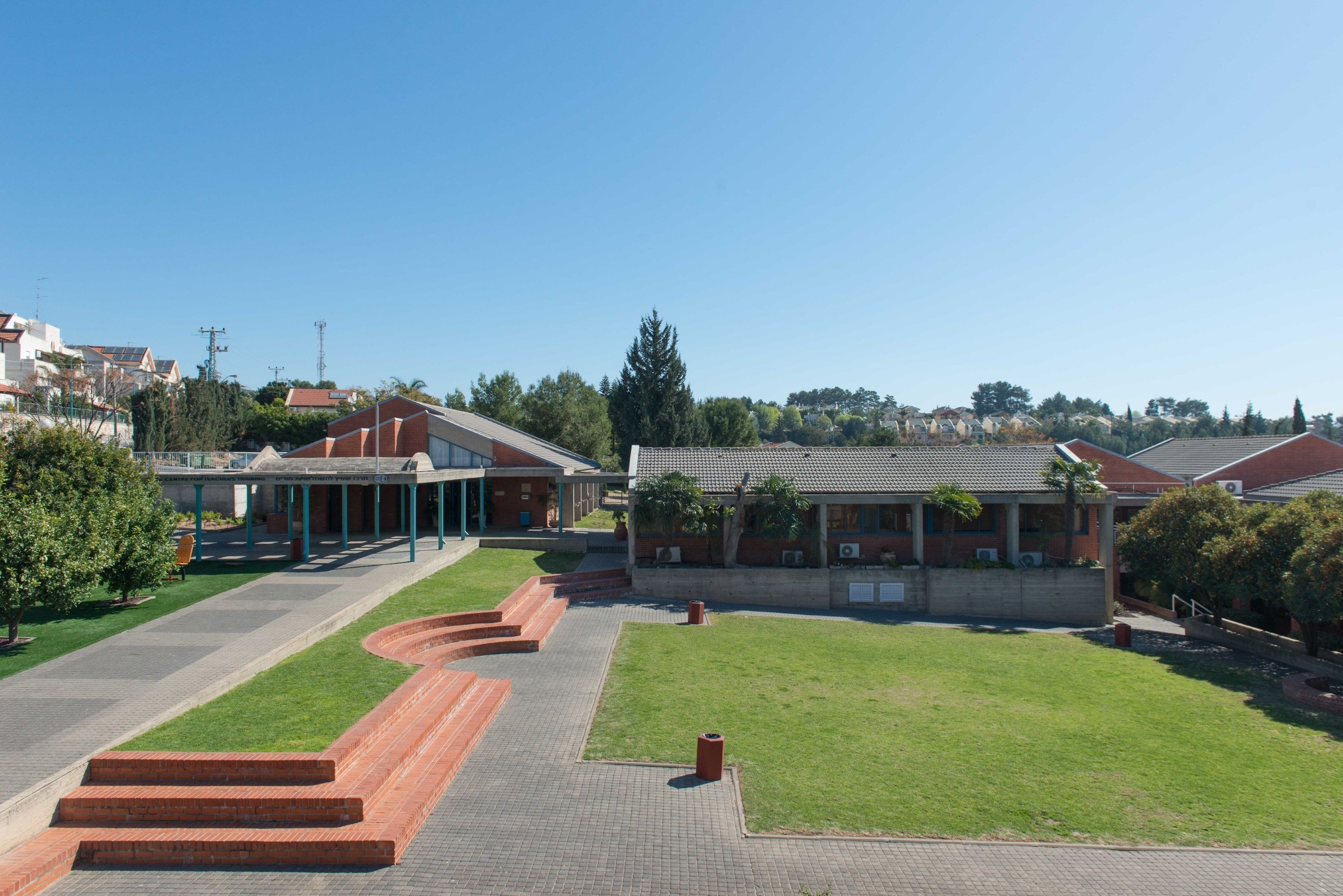 Pátio com gramado central, caminho de tijolos e edifícios com telhados vermelhos e janelas.