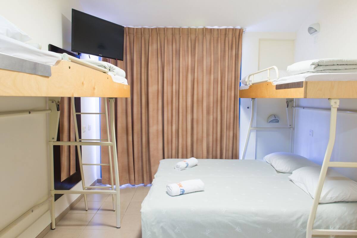 A hotel room with bunk beds, a TV, a ladder, and a curtain.