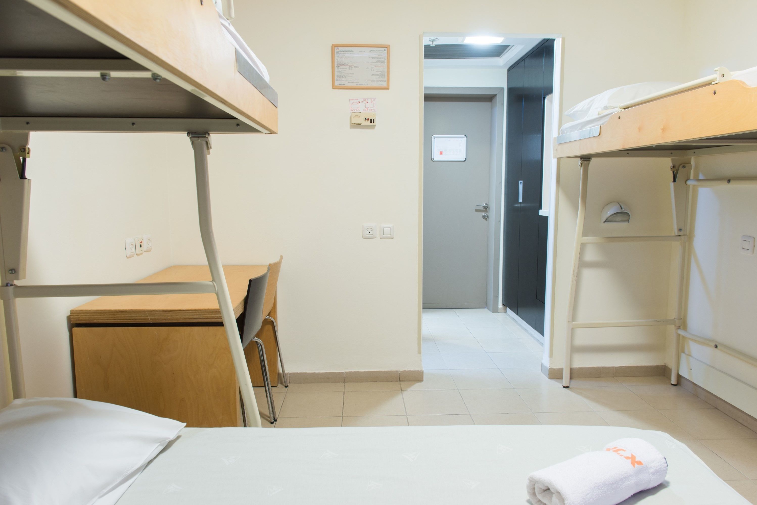 Habitación tipo dormitorio con literas, un escritorio y una silla. Se observa una puerta que conduce a otra habitación.