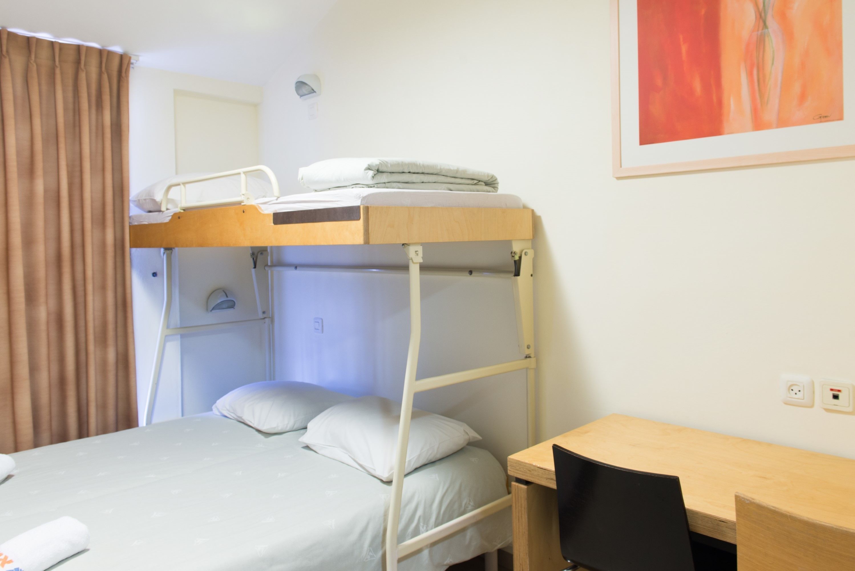 A bunk bed with a desk and chair, a single bed, and a painting on the wall.