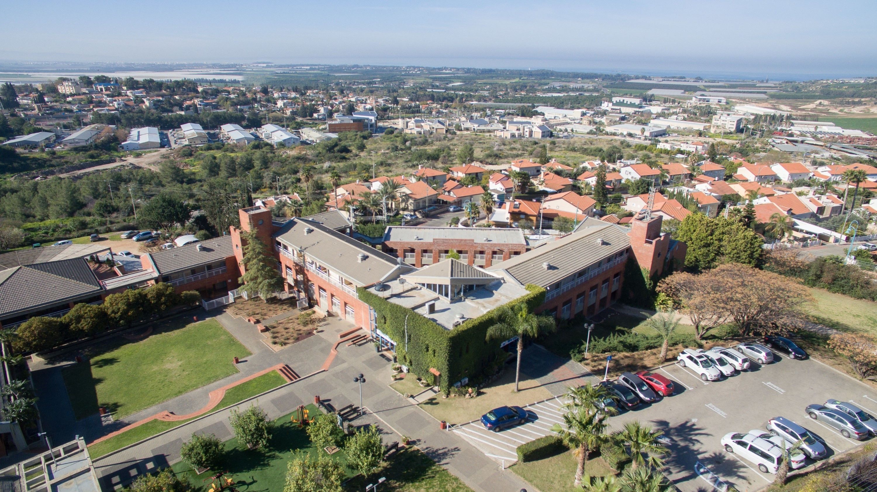 An aerial view of a residential area with a prominent red-brick building, surrounded by houses with red-tiled roofs.
