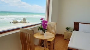 A hotel room with a bed, a small table with chairs, a potted orchid, and a view of the ocean. - Mui Dinh Hotel (Ca Na)