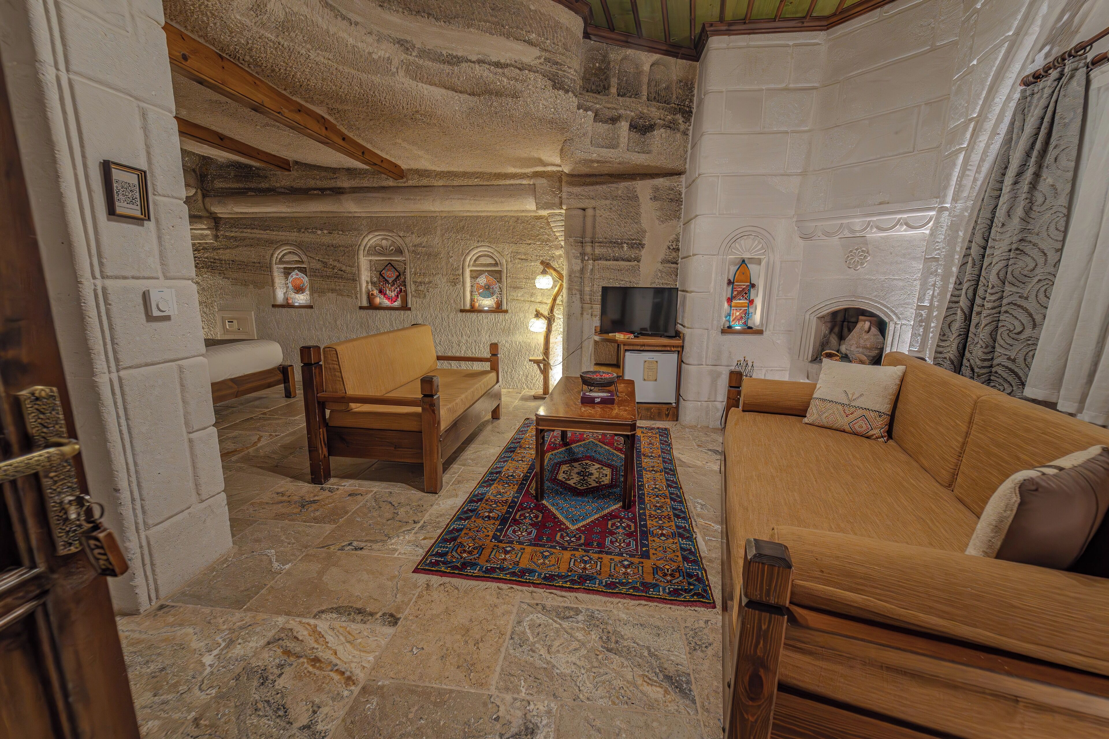 A cozy living room with a stone wall, wooden furniture, a television, and a fireplace.