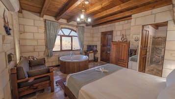 Un dormitorio acogedor con techo de madera, una cama grande, un área de descanso con sofá, una bañera redonda y una ventana con cortinas.