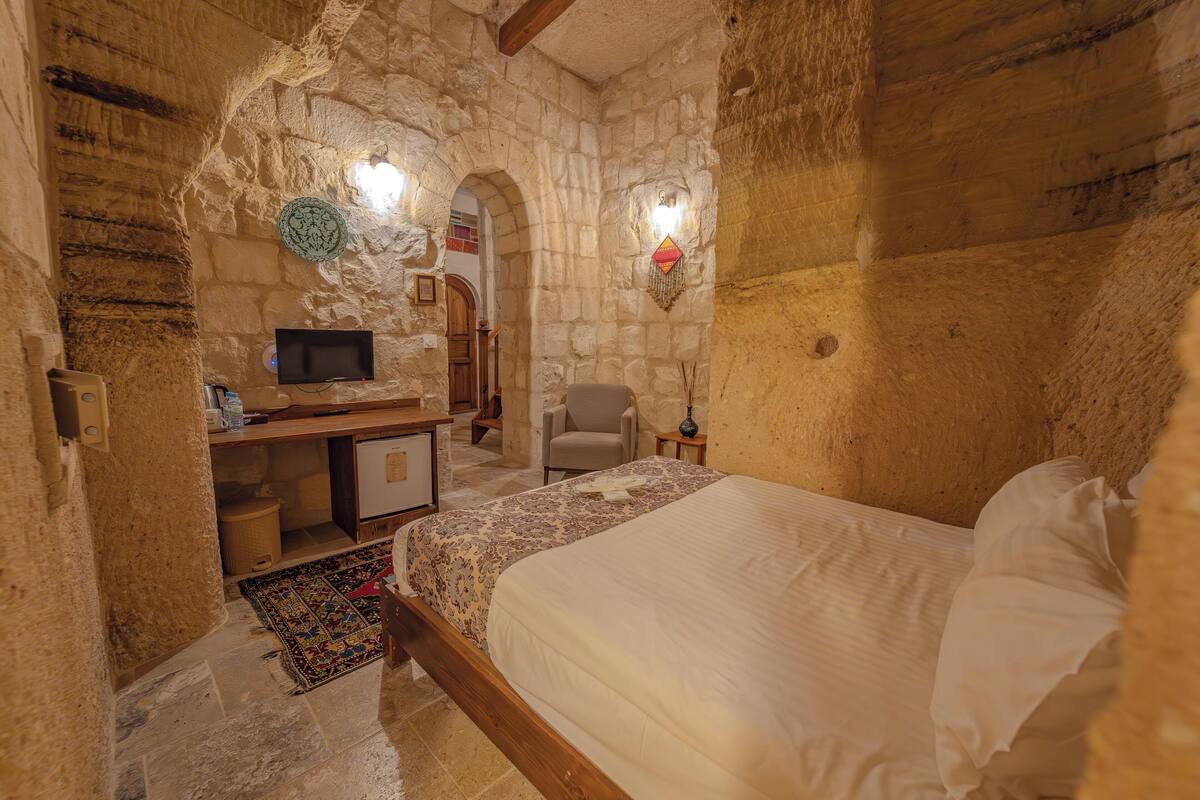 Une chambre aux murs de pierre, avec un lit, un bureau et un téléviseur.