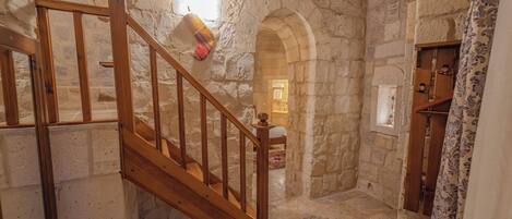 Interior con paredes de piedra y una escalera de madera que conduce a una habitación.