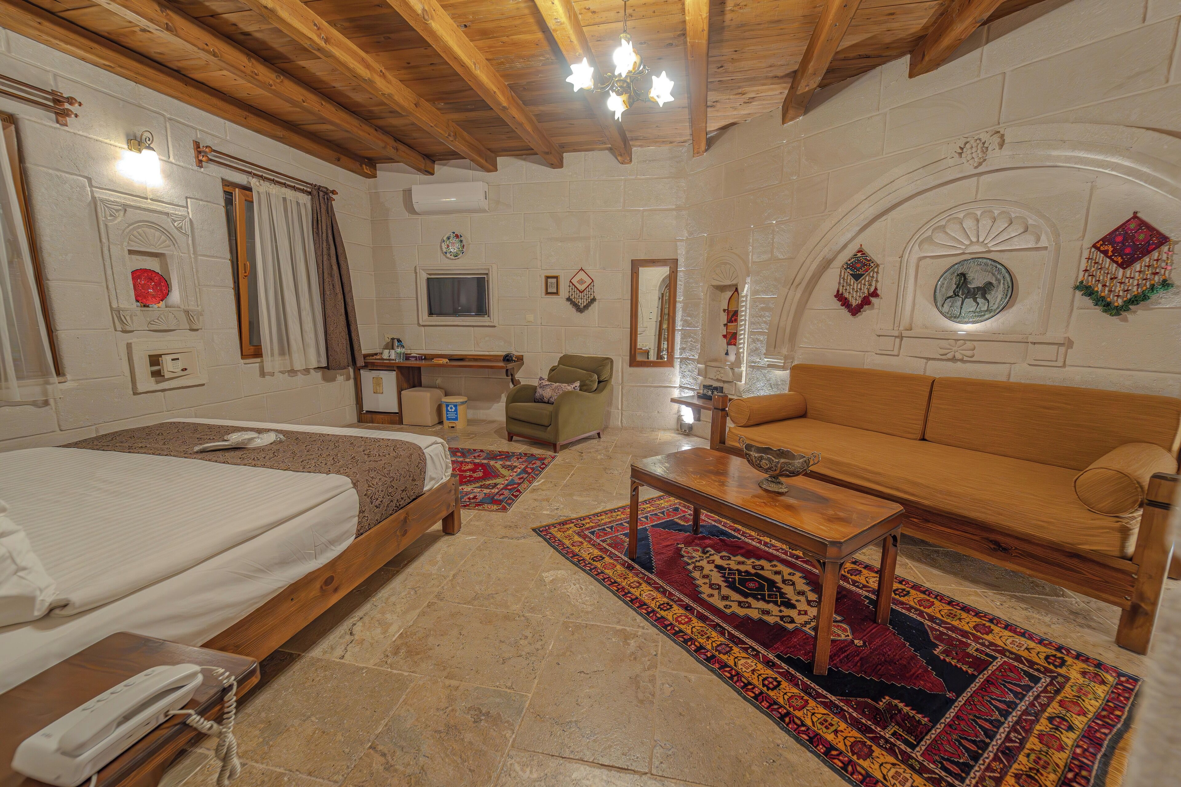 A room with a bed, a sofa, a wooden coffee table, a desk, and a television.