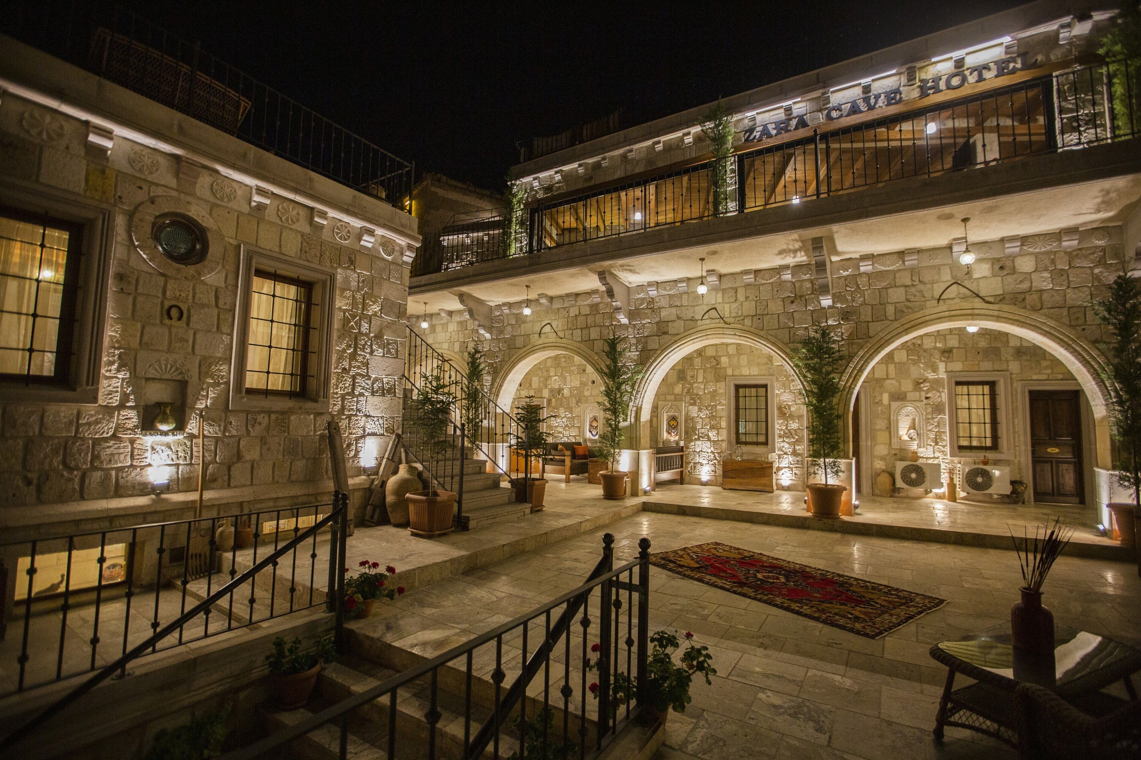 A multi-level stone building with arched doorways, a staircase, and a balcony with a railing.
