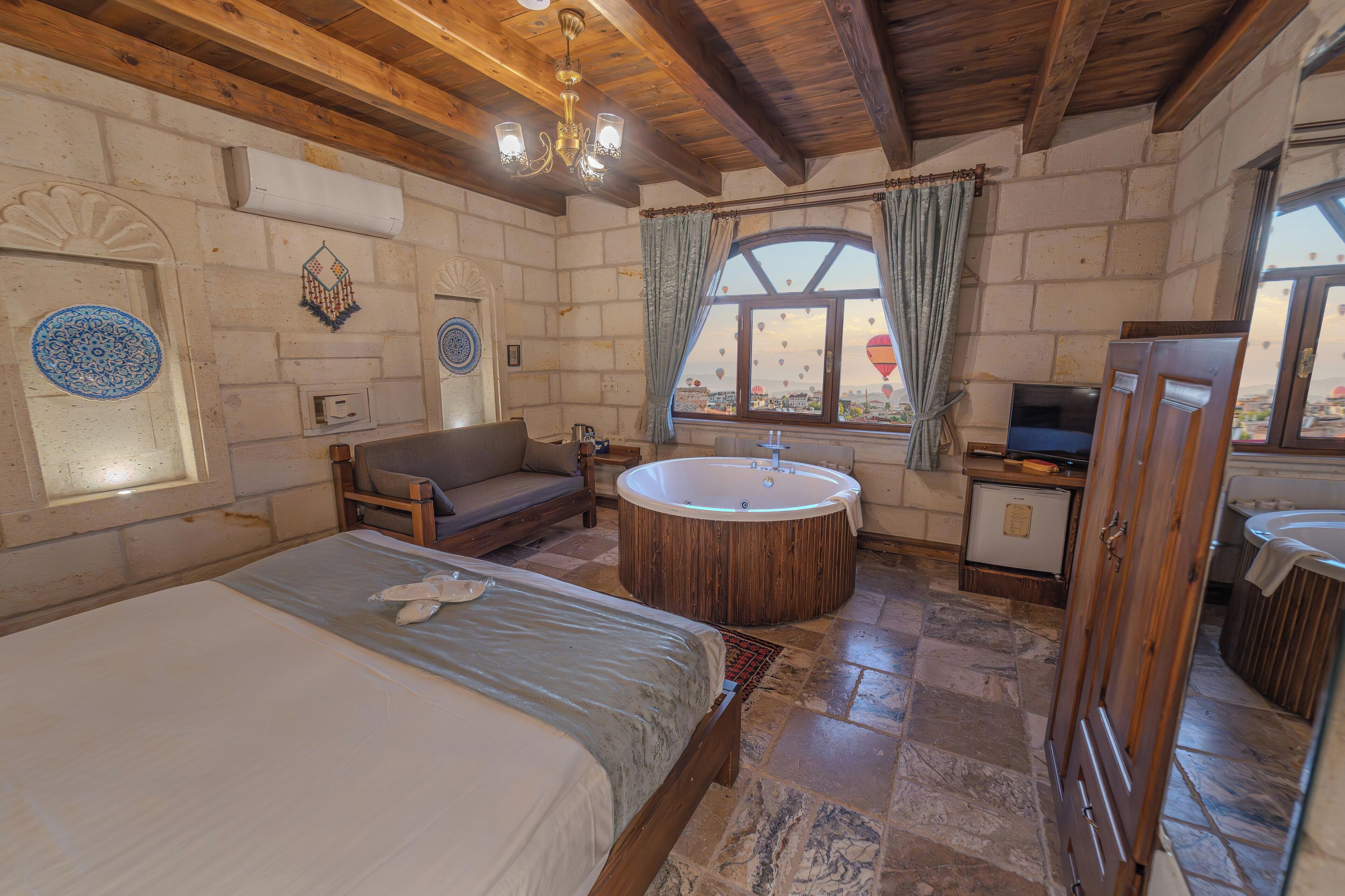 Un dormitorio con una cama grande, techo de madera, bañera y ventana con vistas a globos aerostáticos.