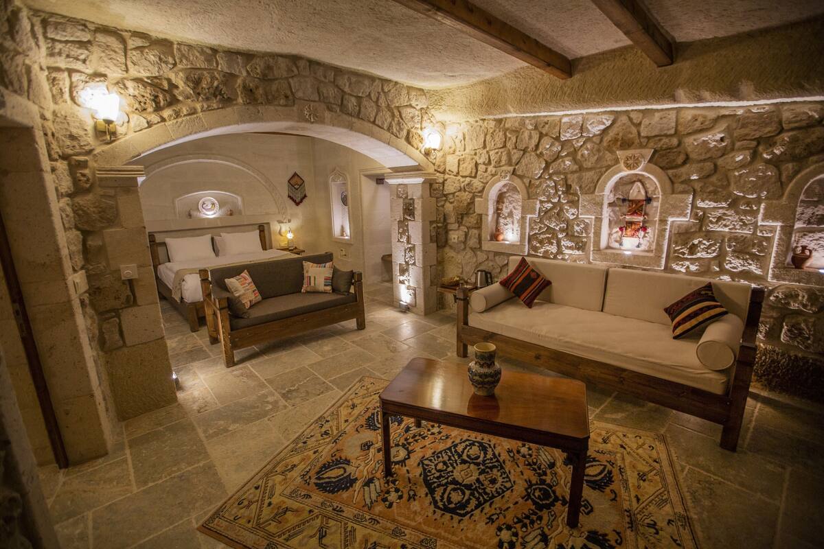 Un salon chaleureux avec des murs en pierre, un canapé, une table basse en bois et un tapis à motifs.