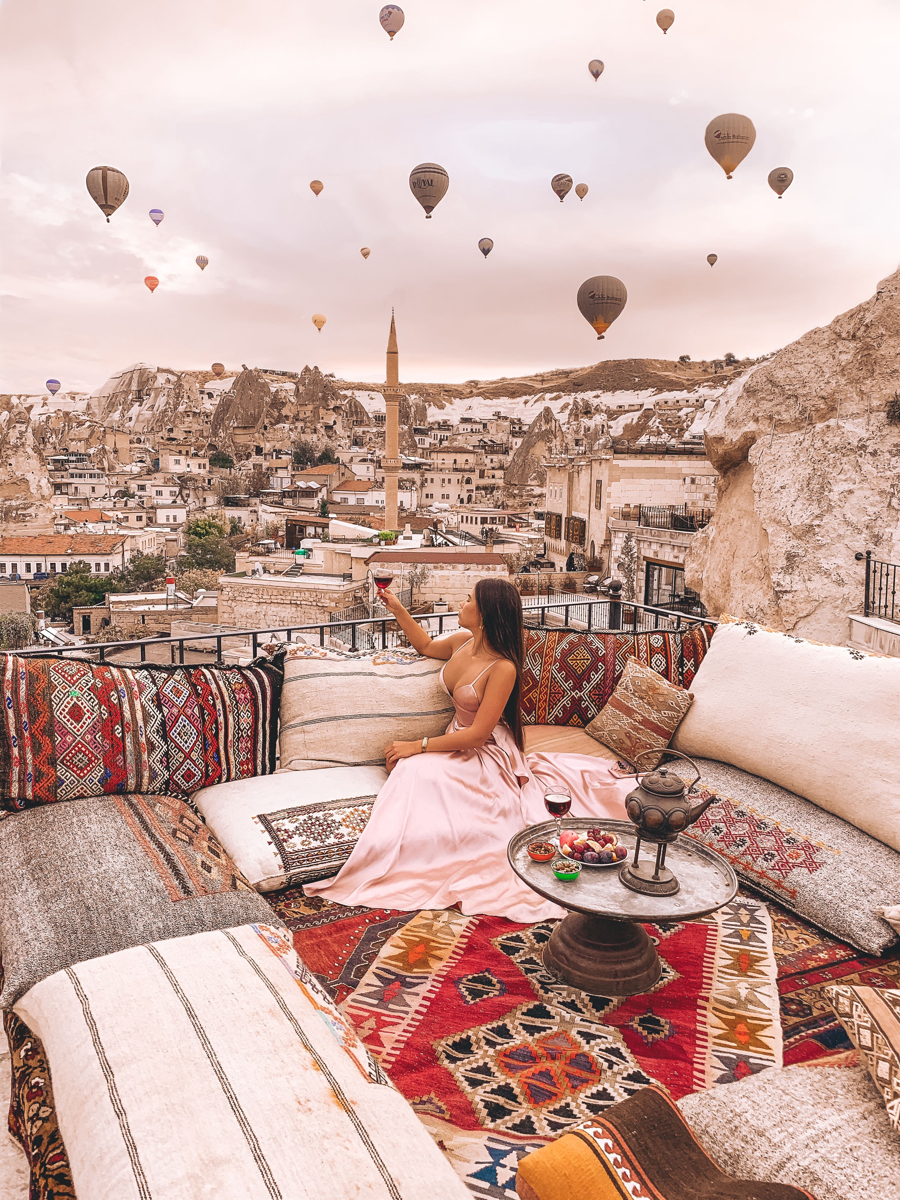 Eine Frau sitzt auf einem Sofa mit Blick auf eine Skyline und Heißluftballons am Himmel.