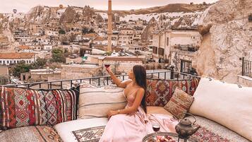 A woman sitting on a sofa with a view of a cityscape and hot air balloons in the sky.