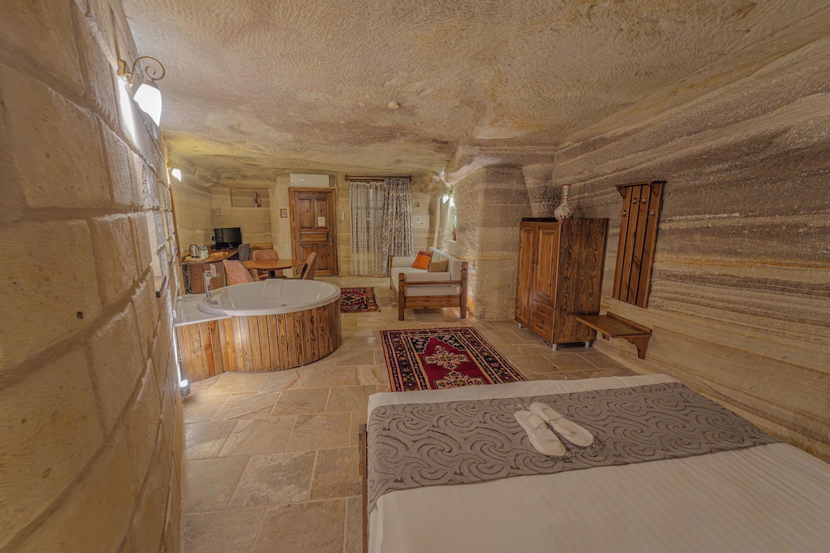 Une pièce avec un mur en pierre, une baignoire en bois, un lit recouvert d’une courtepointe à motifs, une chaise en bois et un meuble en bois.