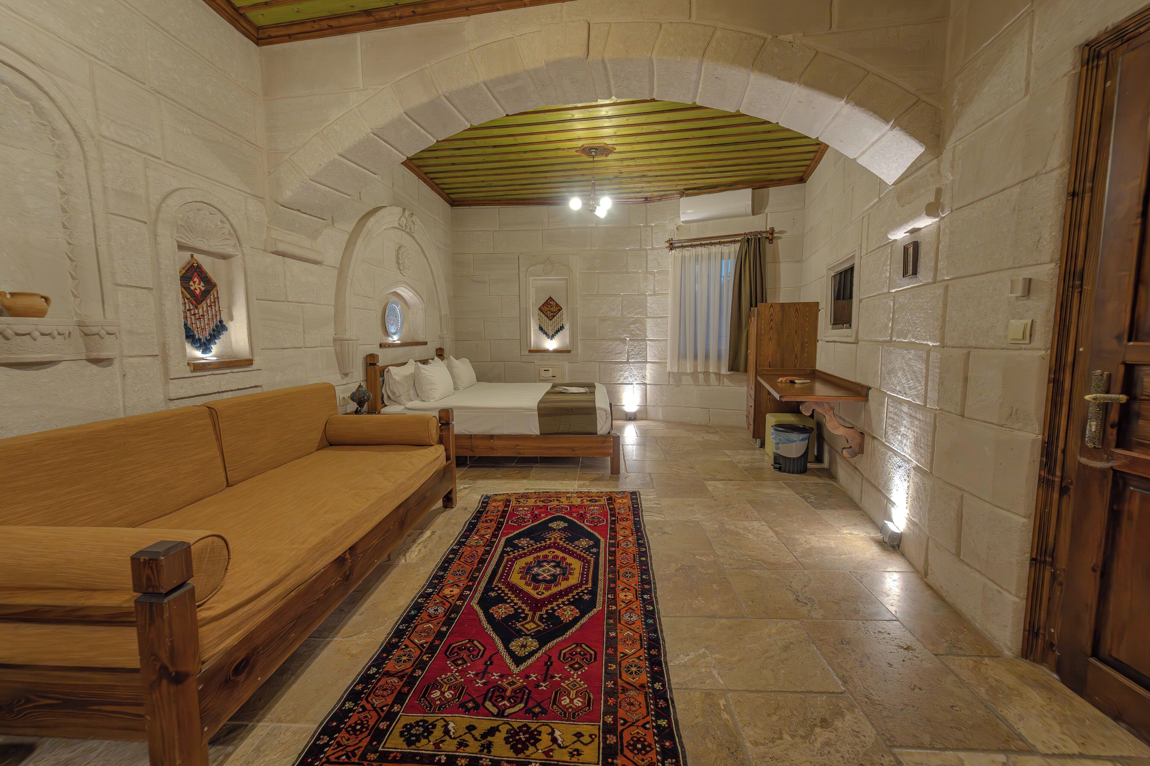 Una habitación con sofá de madera, cama con alfombra estampada, paredes de piedra y puerta de madera.