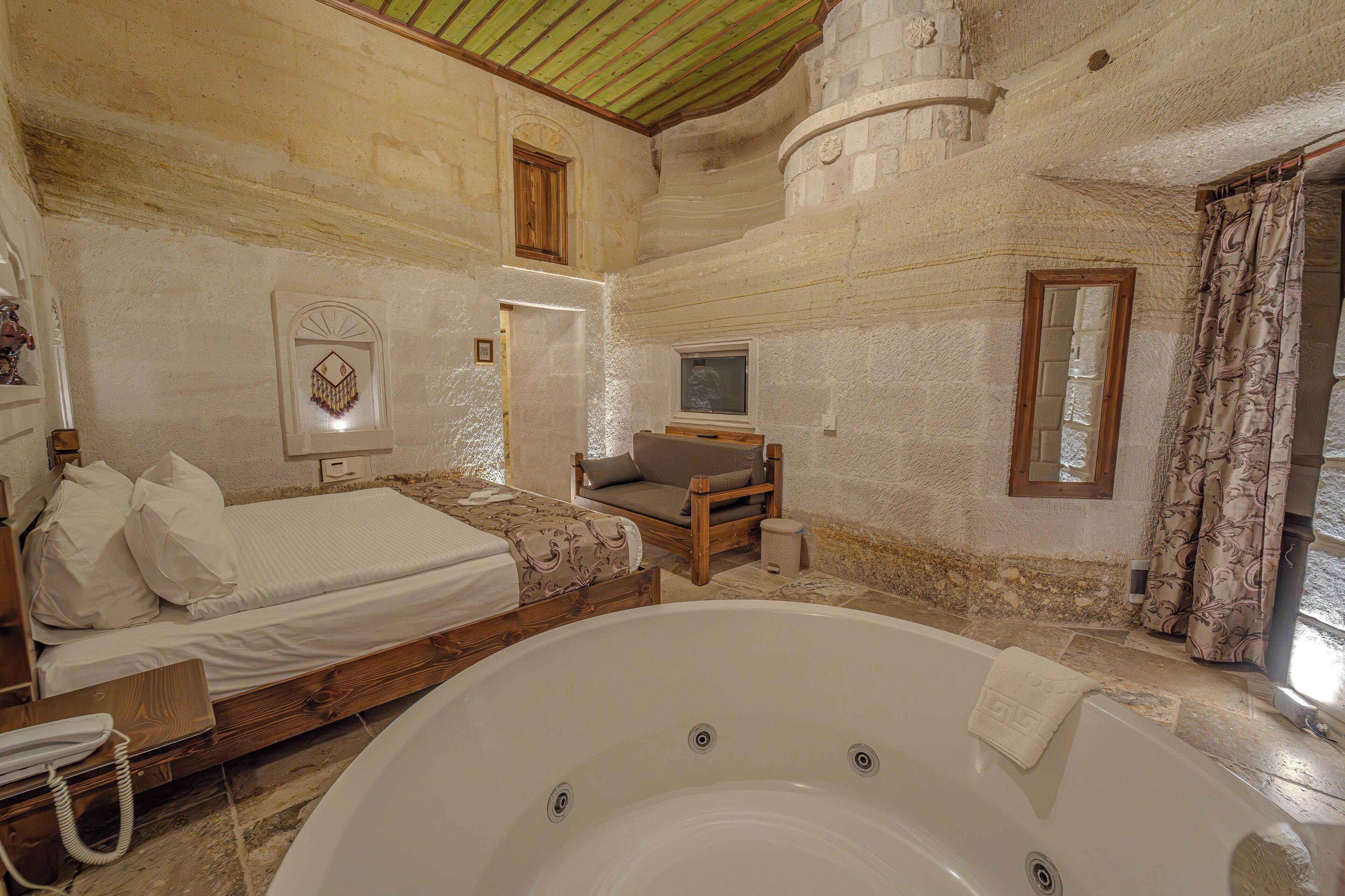 Une chambre à coucher avec une grande baignoire, un lit recouvert de draps blancs, une chaise en bois et une petite fenêtre.