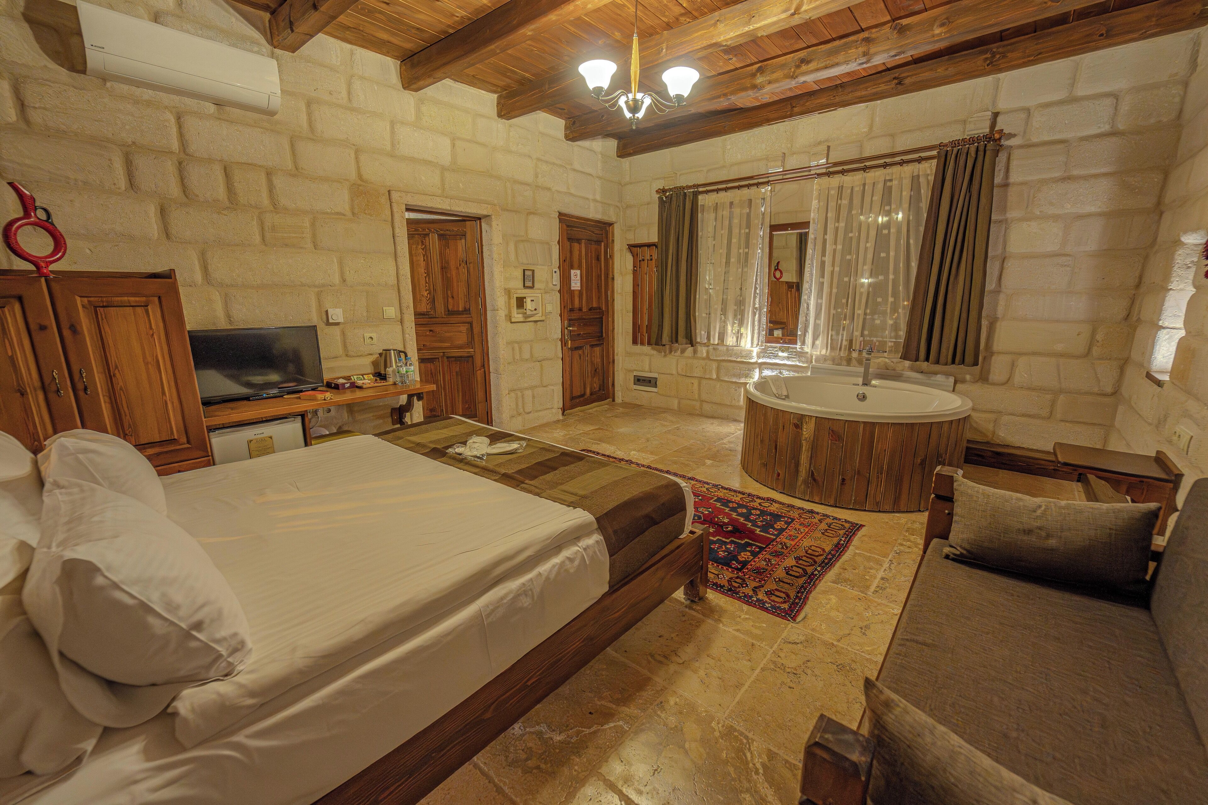 Un dormitorio con cama, cómoda de madera, televisor, mesa de madera redonda, sofá y baño con lavamanos y espejo.