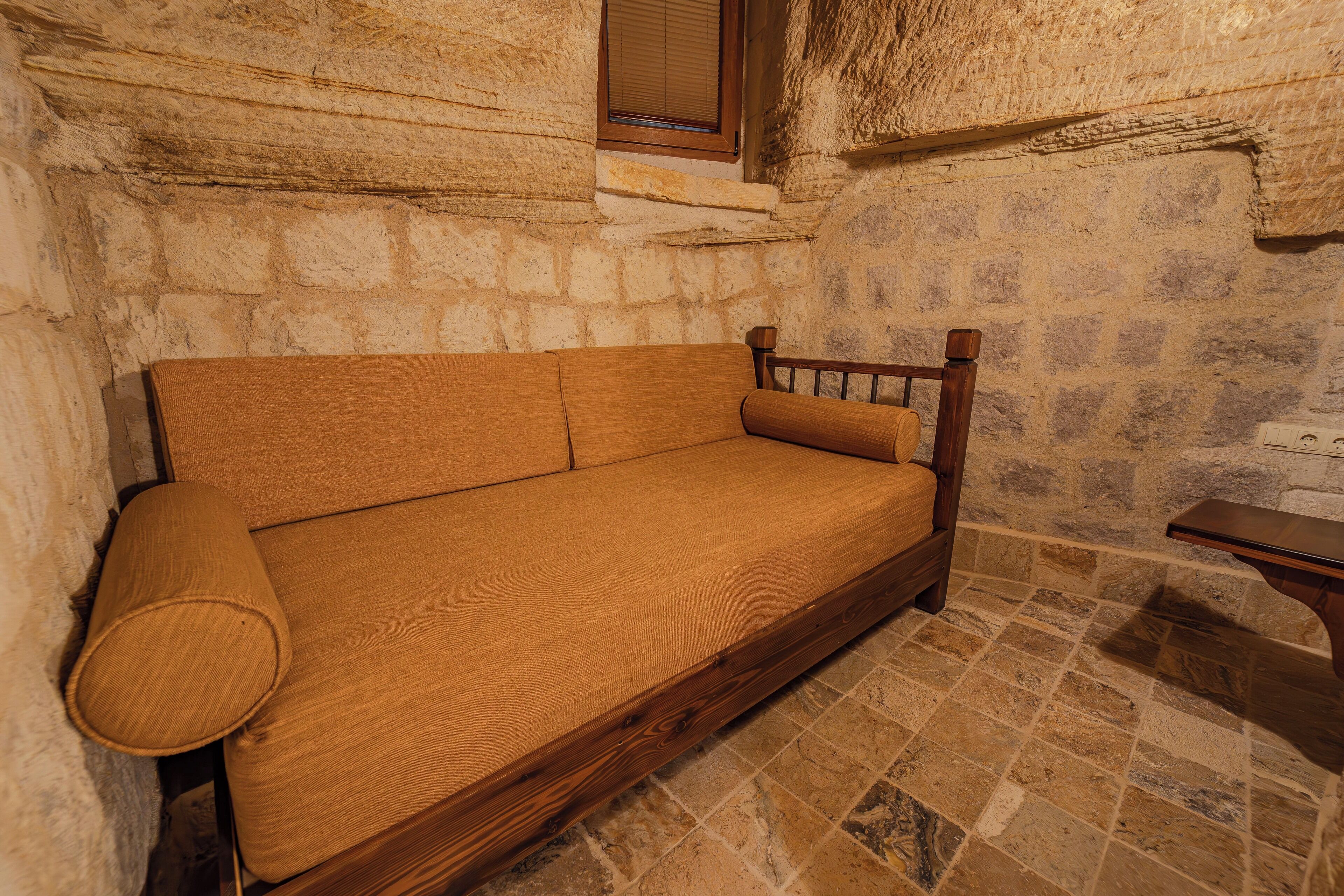A wooden sofa in a stone-walled room with a tiled floor.