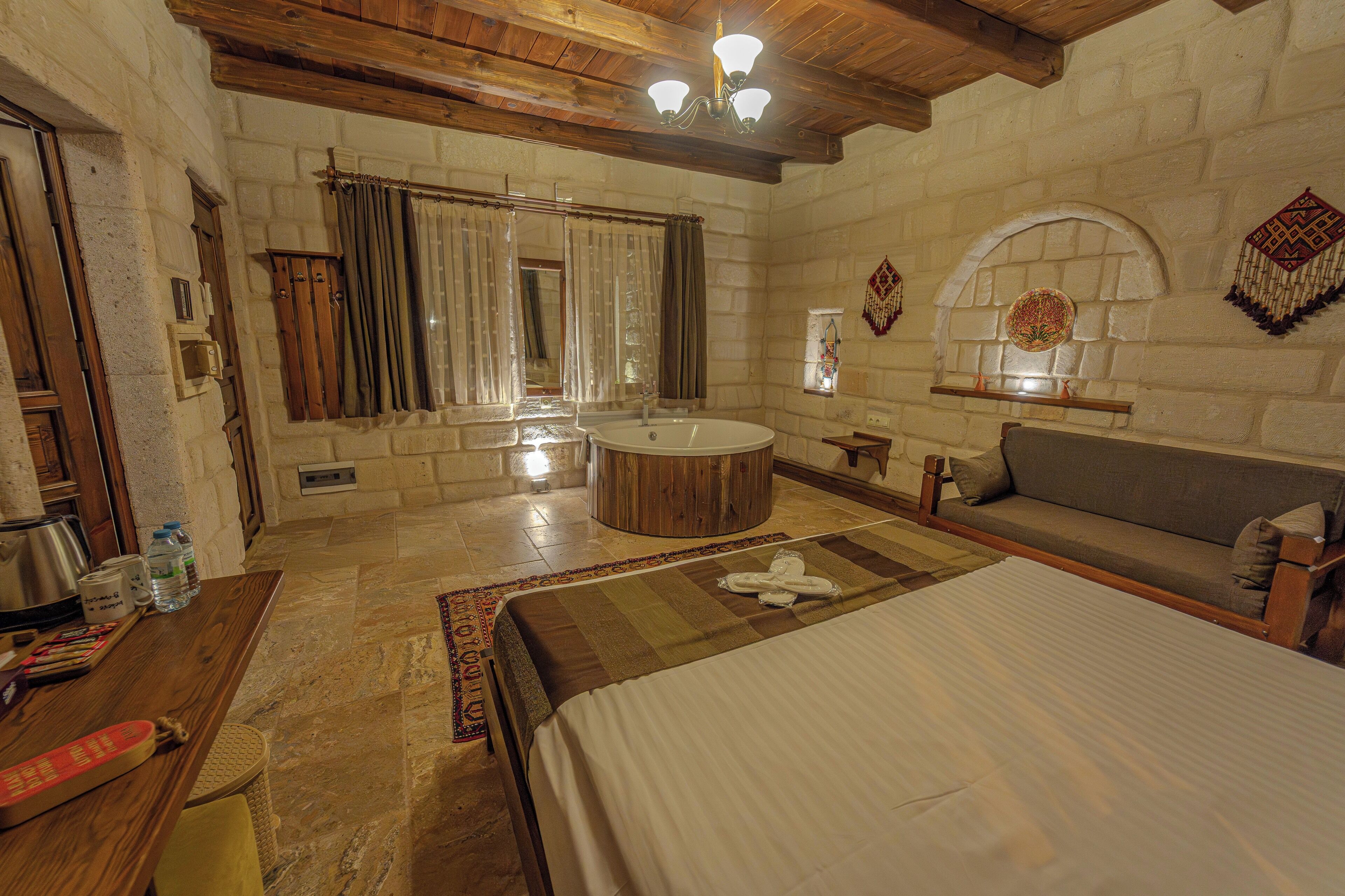 A room with a large bed, a wooden ceiling, a stone wall, a bathtub, and a sofa.