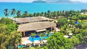 A resort with a pool, thatched-roof structures, and palm trees. - Anh Minh Manchester (Nha Trang)