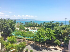 A resort with a pool area, surrounded by lush greenery and palm trees, overlooking a clear blue sea. - Anh Minh Manchester (Nha Trang)