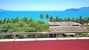 A coastal view with a clear blue sea, palm trees, and a building with a thatched roof. - Anh Minh Manchester (Nha Trang)