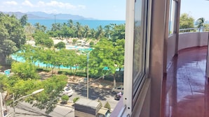 A view from a window overlooking a resort area with a pool, palm trees, and a distant mountain range. - Anh Minh Manchester (Nha Trang)