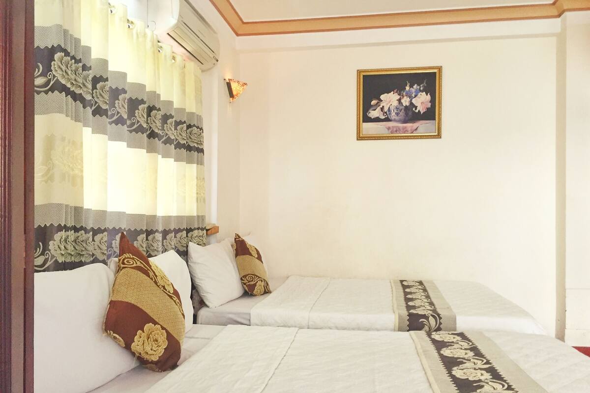 A hotel room with two beds, a decorative curtain, a wall-mounted light, and a framed floral painting.