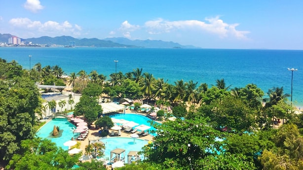 A resort with multiple swimming pools, lush greenery, and a view of the ocean and distant mountains. - Anh Minh Manchester (Nha Trang)