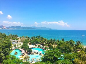 A resort with multiple swimming pools, lush greenery, and a view of the ocean and distant mountains. - Anh Minh Manchester (Nha Trang)