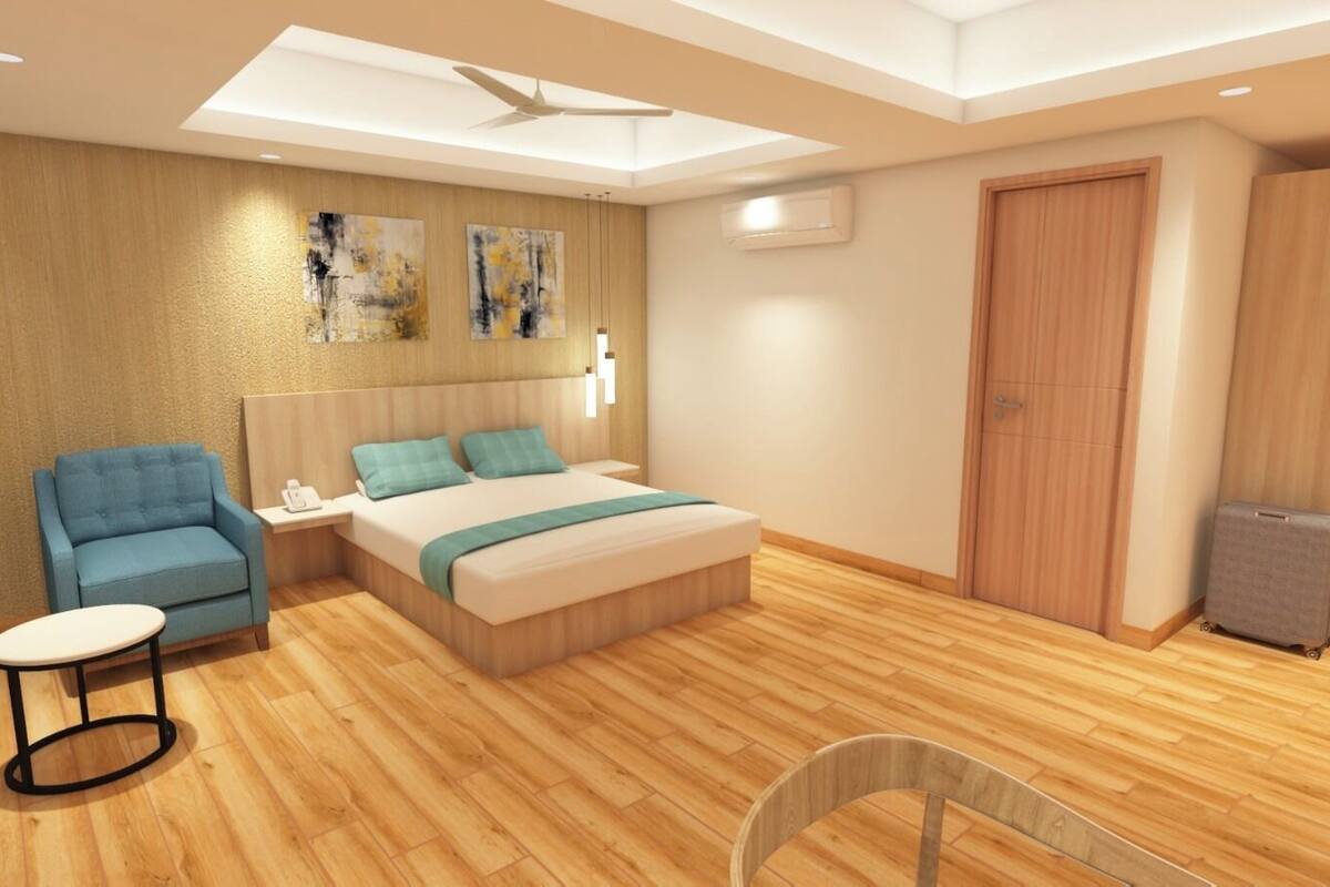 A modern hotel room with a bed, a blue armchair, a small table, a wardrobe, and an air conditioning unit.