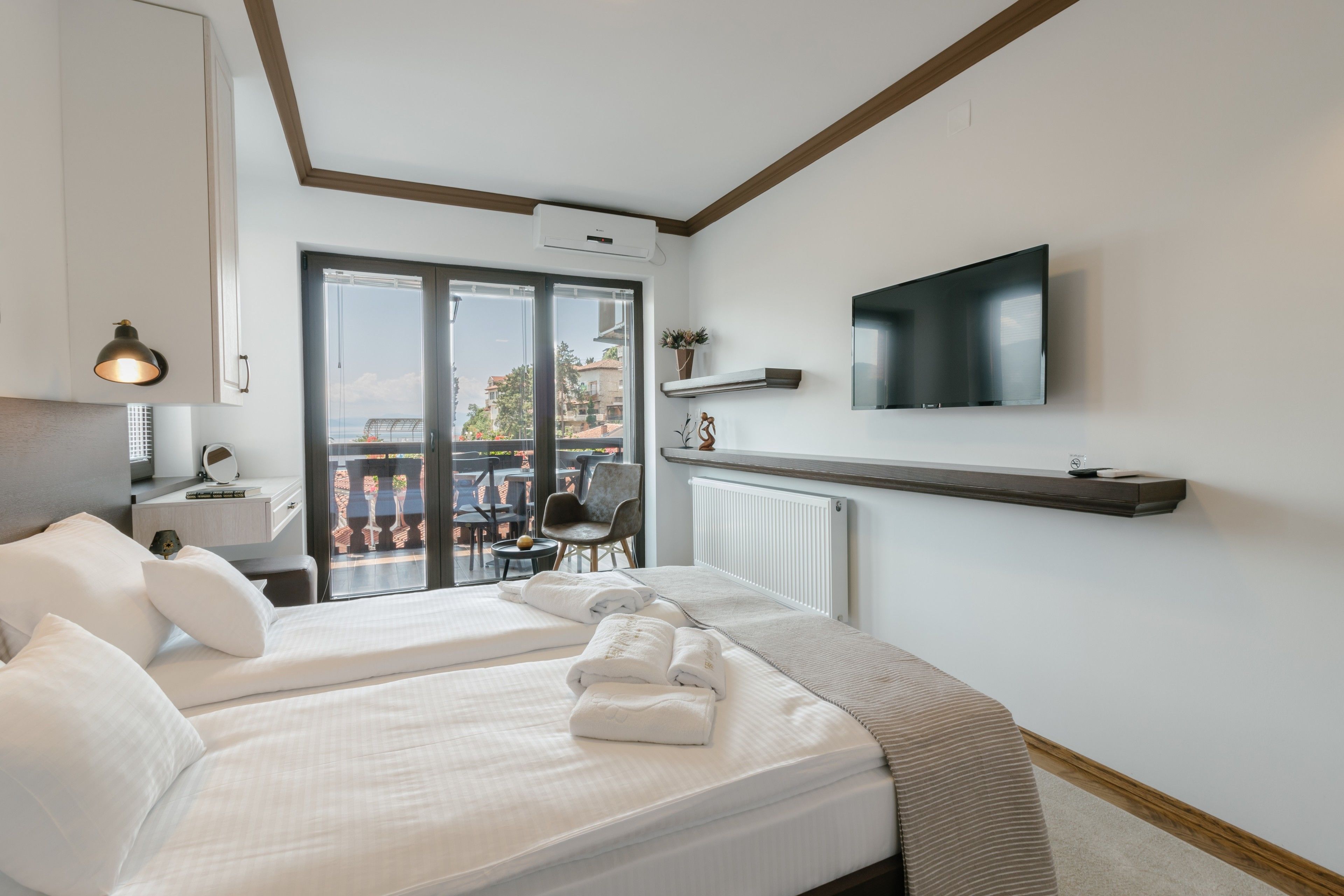 Une chambre d’hôtel avec un lit, un téléviseur fixé au mur, un balcon avec une chaise et une vue sur la ville.
