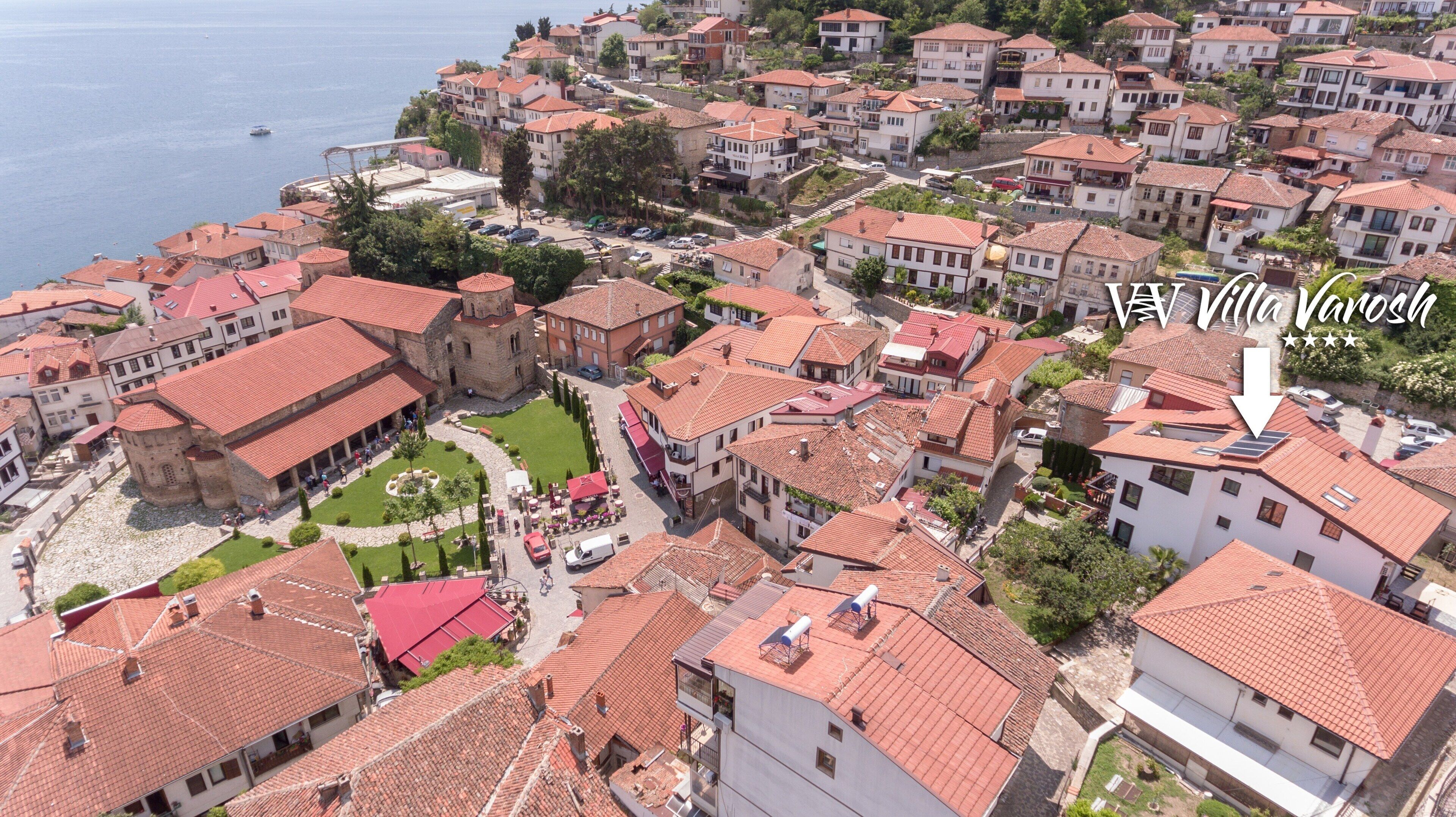 An aerial view of a coastal town with red-tiled buildings, a central courtyard, and a prominent tower.