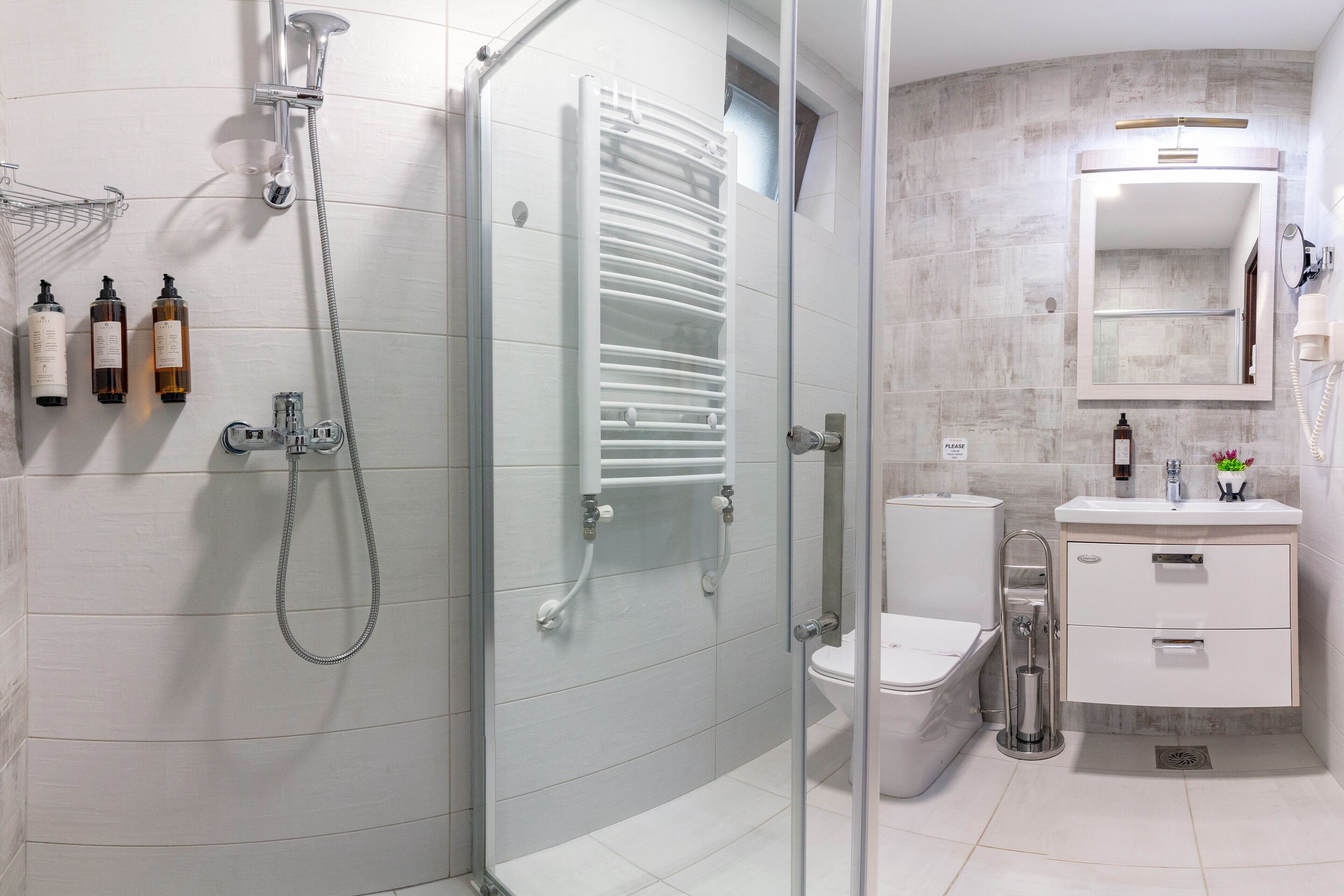 A modern bathroom with a glass-enclosed shower, a toilet, a sink with a mirror, and toiletries on the wall.