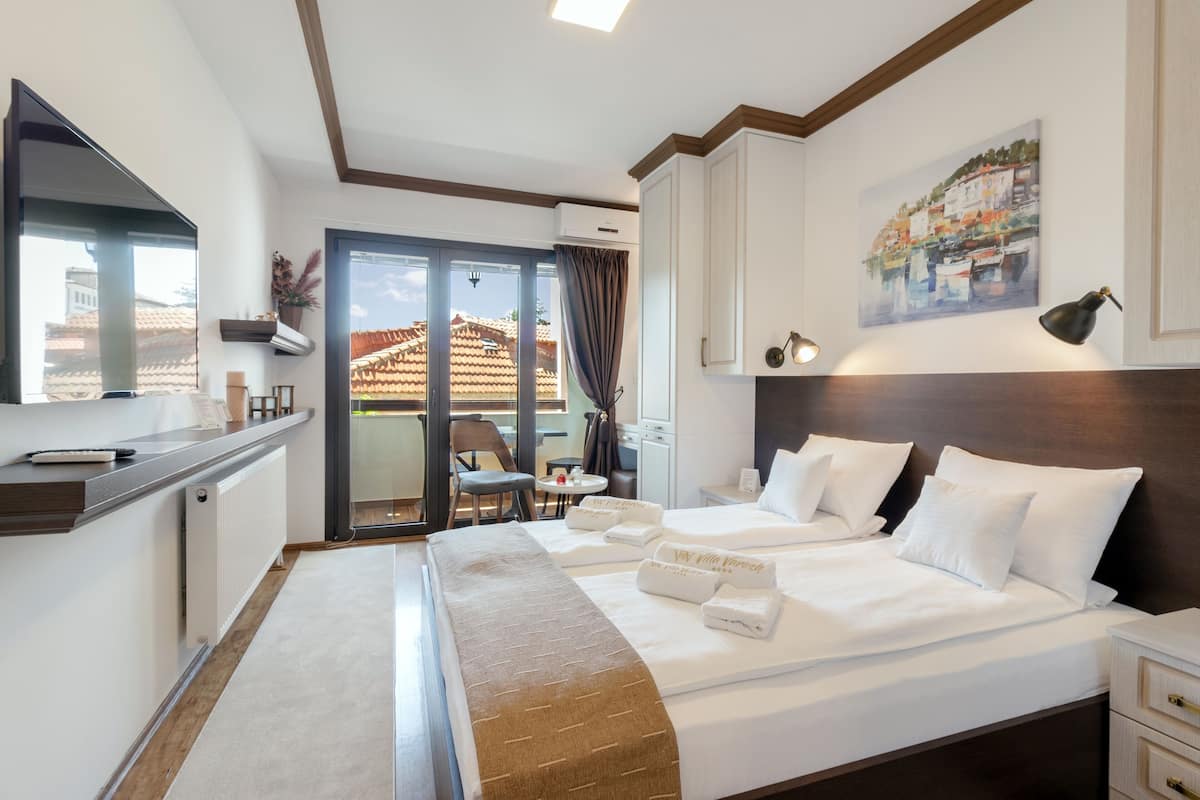 A hotel room with a large bed, a desk, a chair, and a view of the outside.