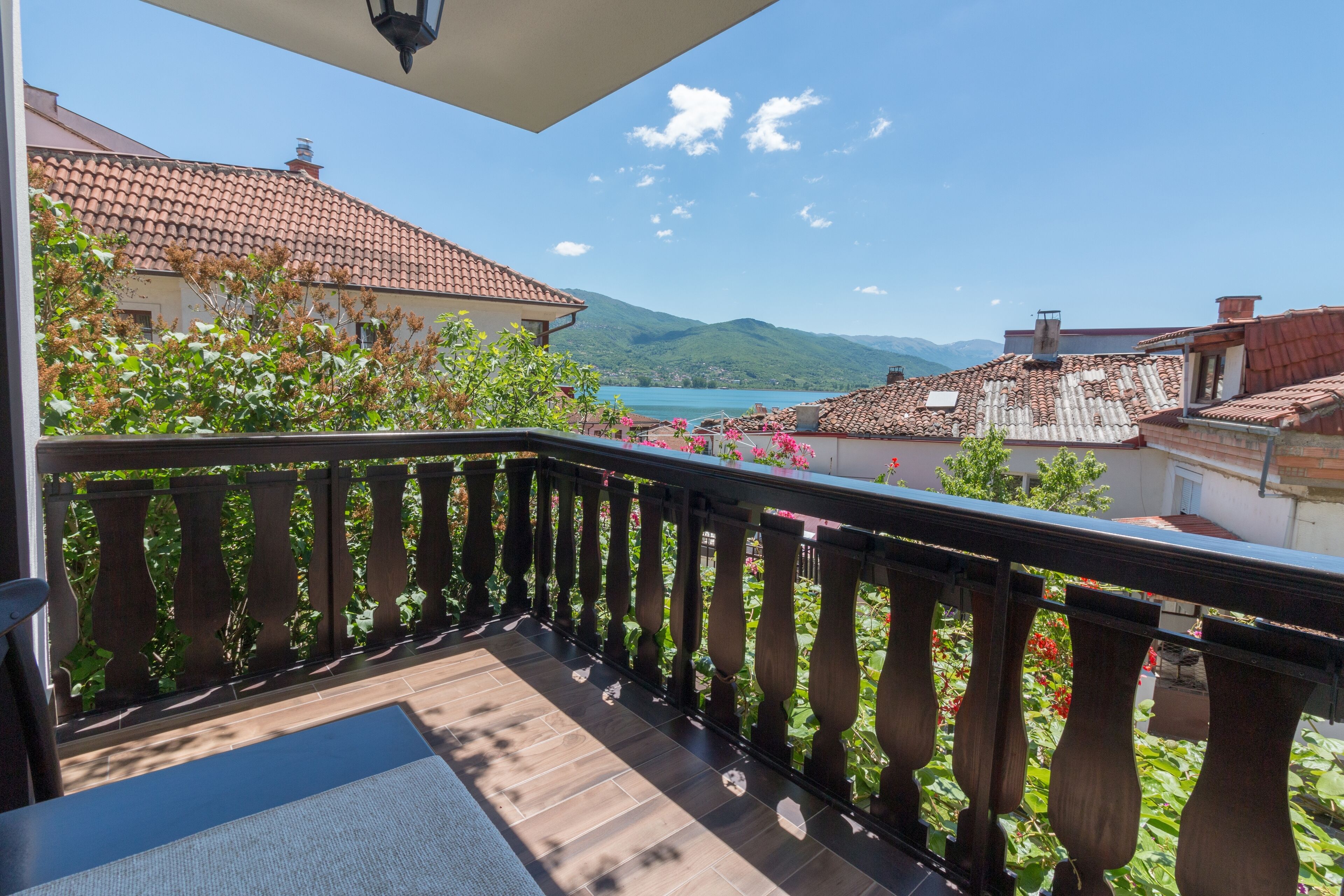 Un balcon offrant une vue sur un lac, des montagnes et des bâtiments aux toits de tuiles rouges.