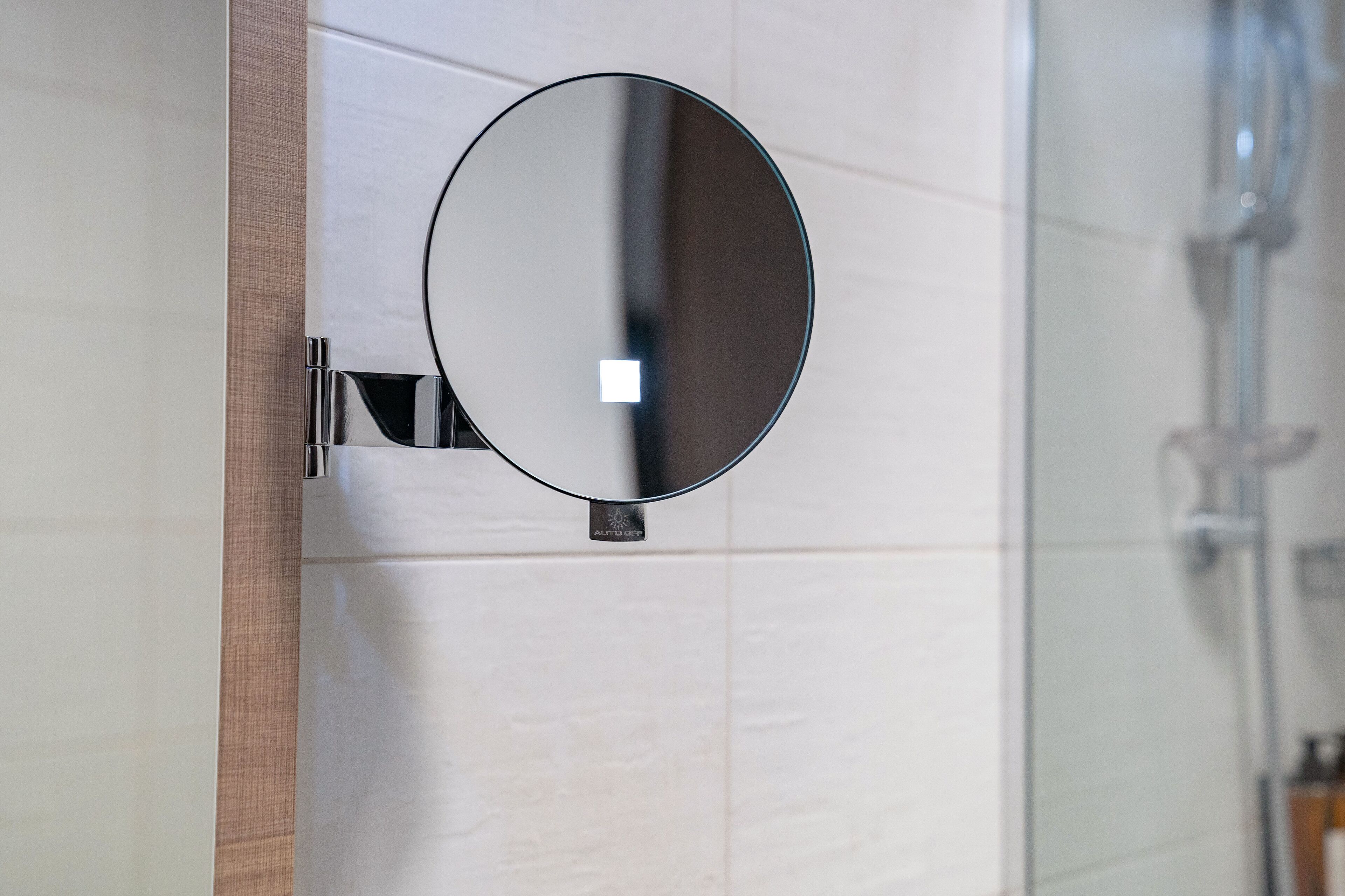 Un baño con un espejo redondo sujeto a una pared con azulejos blancos.