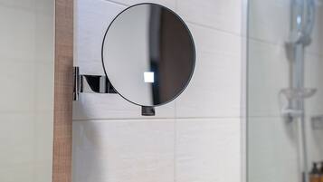 Un baño con un espejo redondo sujeto a una pared con azulejos blancos.