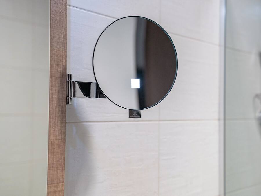 Un baño con un espejo redondo sujeto a una pared con azulejos blancos.