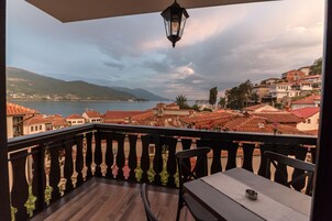 Un balcón con vistas al mar y a las montañas, suelo de madera y una mesa con sillas.